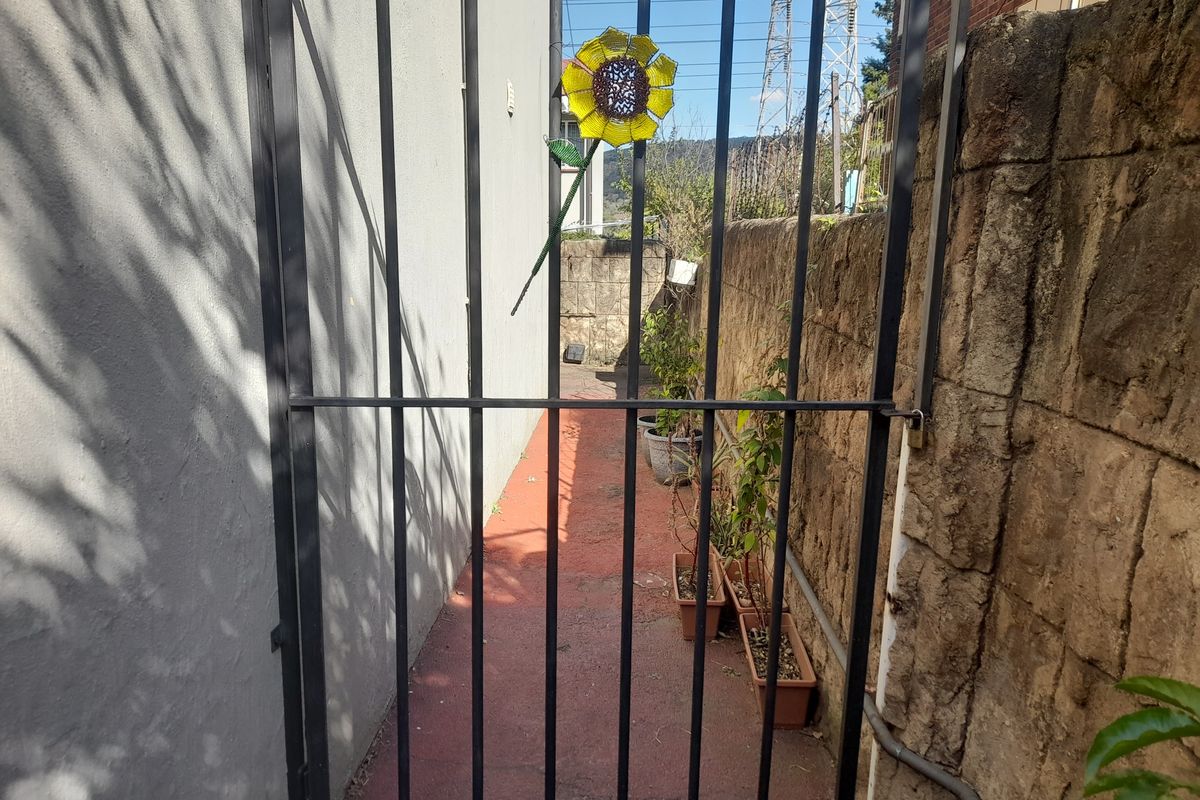 A narrow side passage featuring a metal security gate, stone retaining wall, and paved walkway.