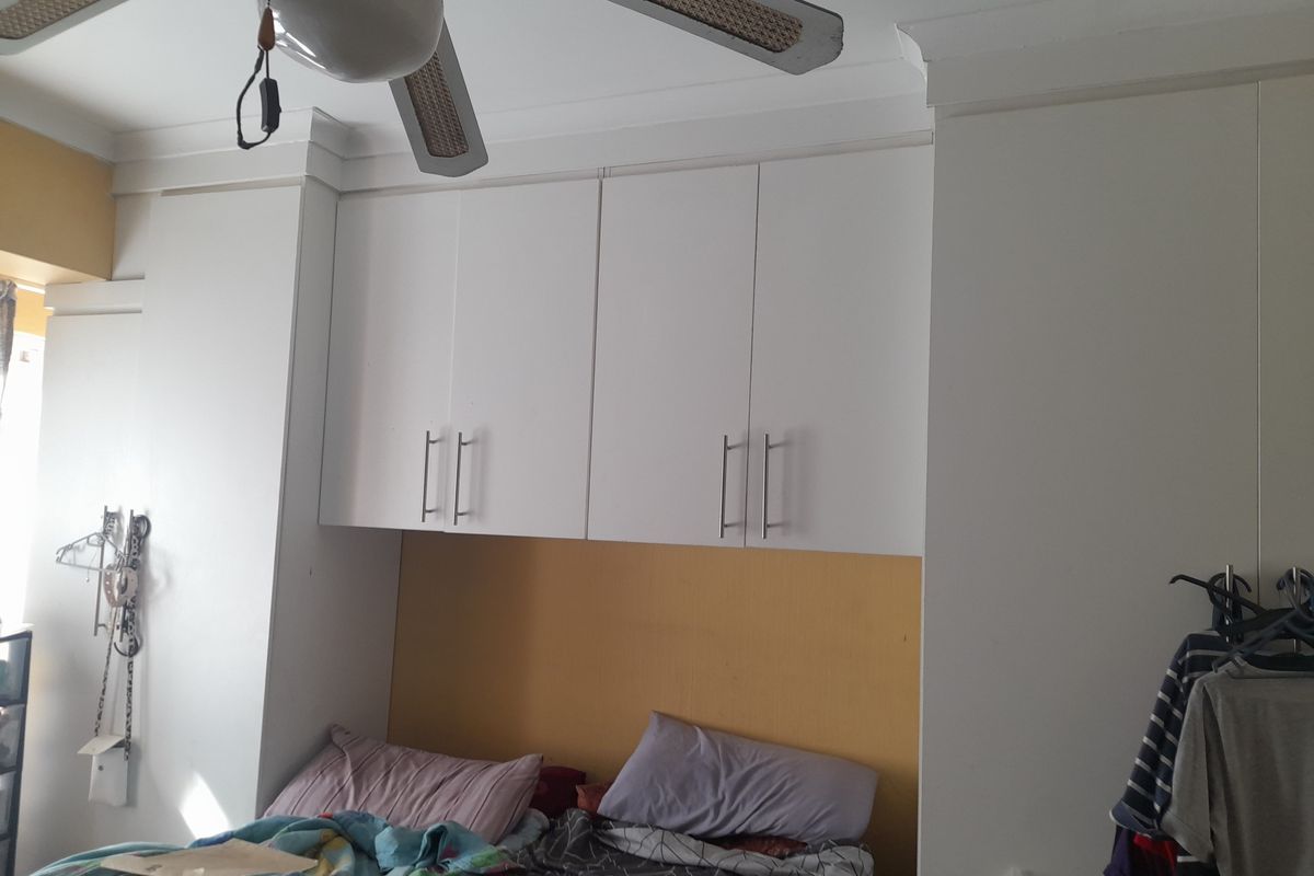 A bedroom featuring built-in white cabinetry surrounding a central wall section and a ceiling fan.