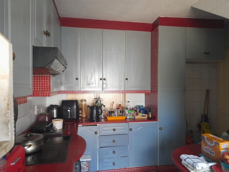A functional kitchen featuring grey cabinetry, red tiled backsplashes, and a built-in electric hob with an extractor fan.