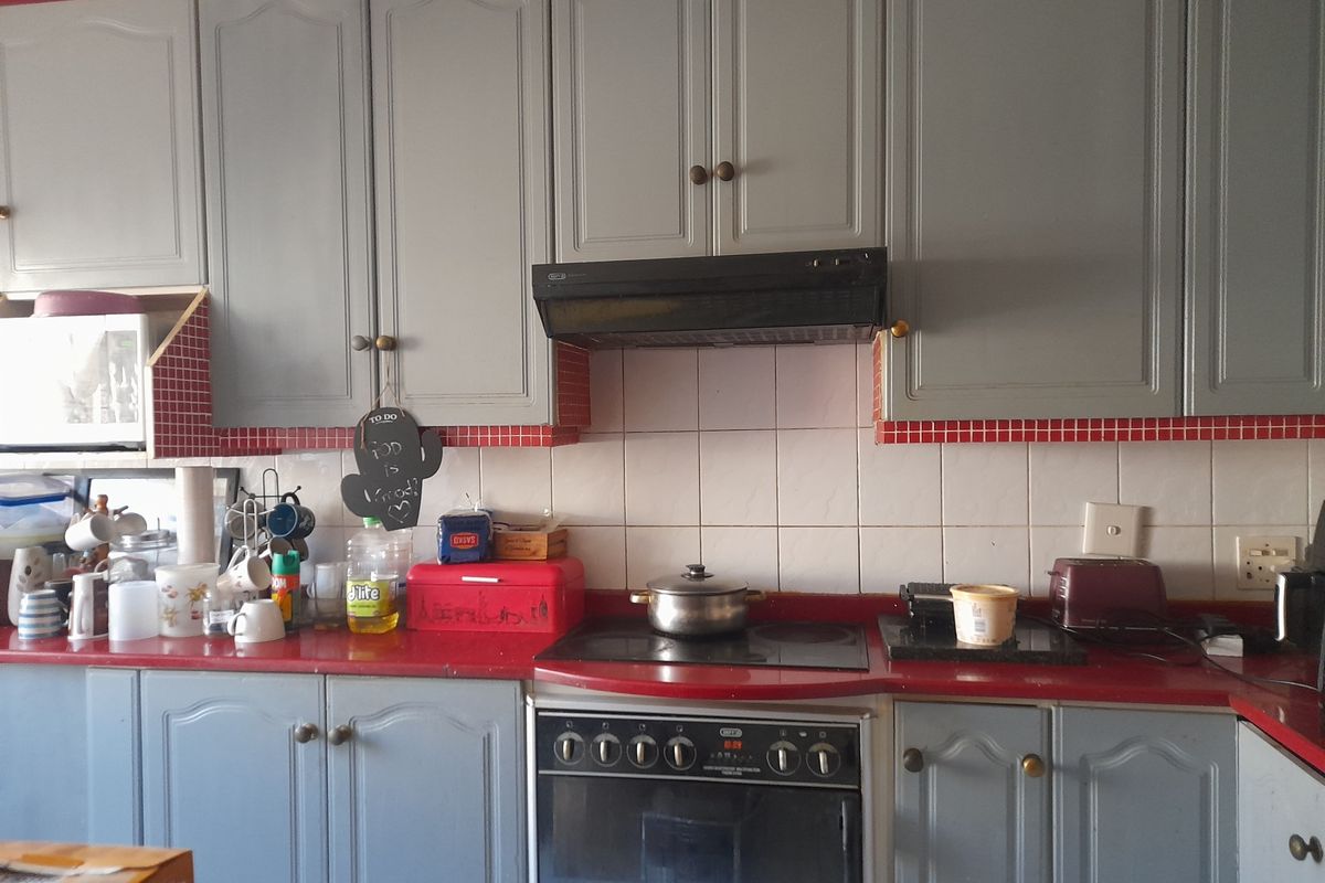 A functional kitchen featuring grey built-in cabinetry, a red countertop, and a built-in electric oven with an extractor fan.