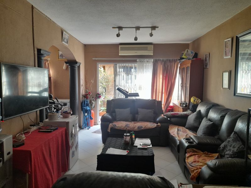 A living room featuring tiled floors, an air conditioning unit, and an archway leading to an outdoor area with a security gate.
