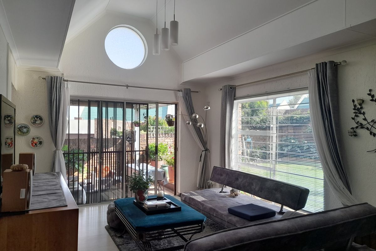 Bright living room featuring a vaulted ceiling, circular window, and large sliding glass doors that provide seamless access to the outdoor patio area.