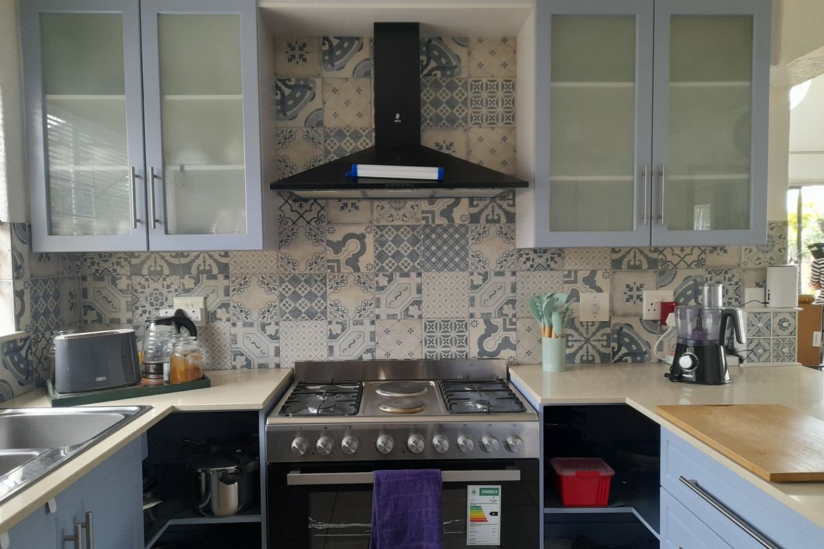 A well-maintained kitchen featuring a gas stove, extractor fan, patterned tile backsplash, and ample built-in cabinetry with glass-fronted upper units.