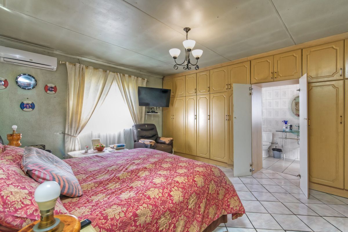 Spacious bedroom featuring extensive built-in wooden cabinetry, an en-suite bathroom, and a wall-mounted air conditioning unit.