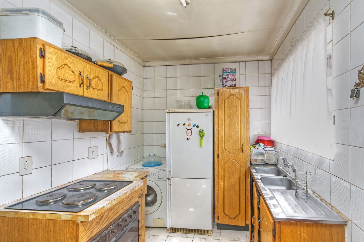 A functional kitchen featuring wooden cabinetry, a built-in electric hob and oven, double stainless steel sink, and tiled walls.