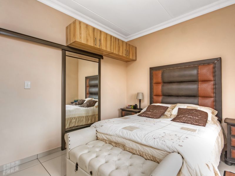 A well-maintained bedroom featuring tiled flooring, crown molding, and built-in wardrobe storage with integrated overhead cabinetry.