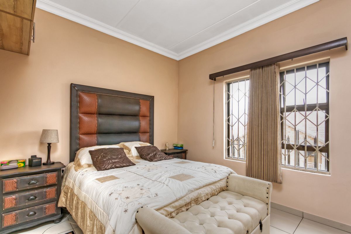A well-lit bedroom featuring tiled flooring, neutral wall tones, and windows fitted with security bars.