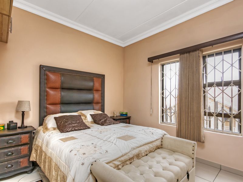 A well-lit bedroom featuring tiled flooring, neutral wall tones, and windows fitted with security bars.
