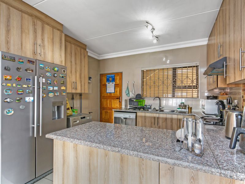A functional kitchen featuring wood-look laminate cabinetry, granite countertops, a tiled backsplash, and a stainless steel sink with a security gate on the door.