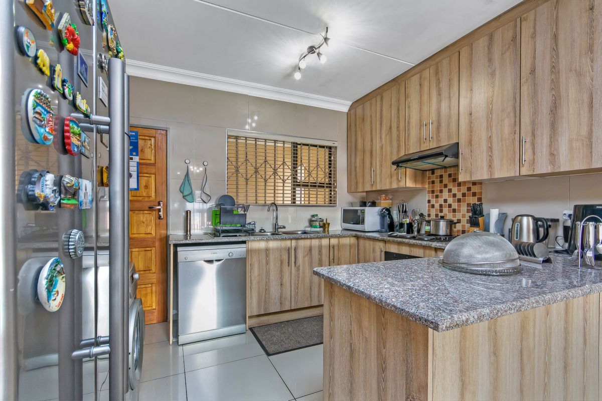 A functional kitchen featuring wood-look laminate cabinetry, granite countertops, tiled flooring, and a tiled backsplash with an integrated extractor fan.