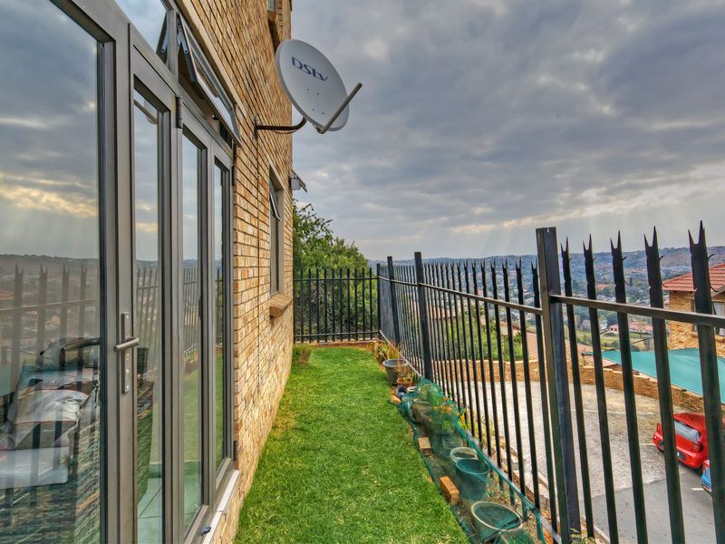 A narrow balcony area featuring brick exterior walls, aluminium glass doors, and metal security fencing overlooking the surrounding neighbourhood.