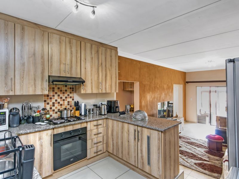 Open-plan kitchen featuring wood-look cabinetry, granite countertops, and built-in appliances, flowing into a living area with direct access to the patio.