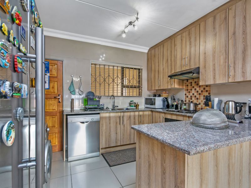 A functional kitchen featuring wood-look laminate cabinetry, granite countertops, tiled flooring, and a tiled backsplash with an integrated extractor fan.