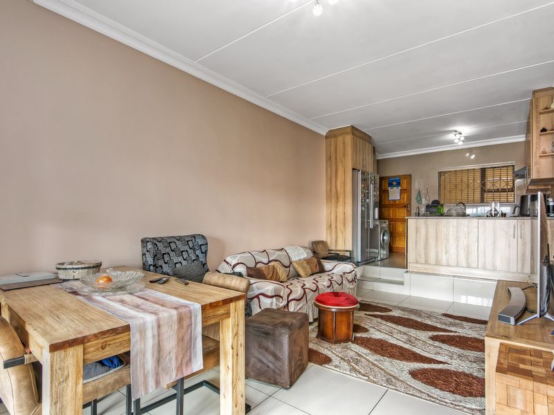 Open-plan living and dining area featuring tiled floors, coved ceilings, and a raised kitchen section with built-in cabinetry.