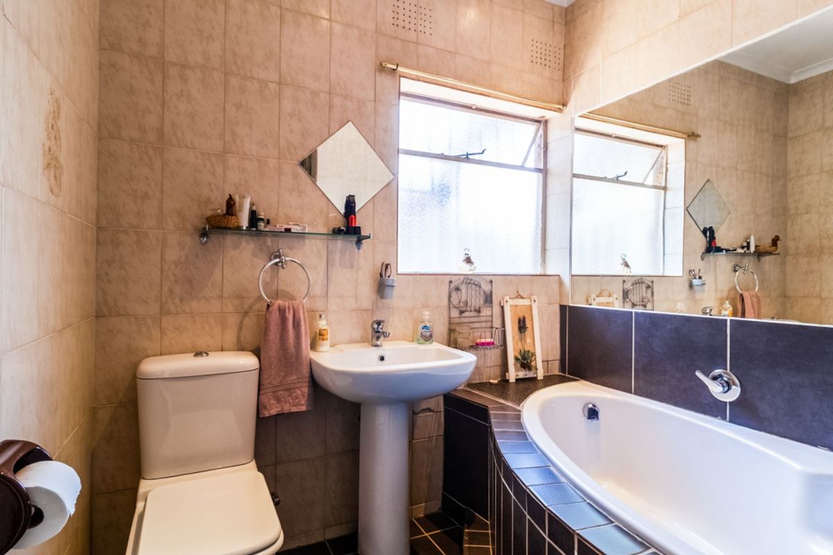 A functional bathroom featuring a pedestal basin, a built-in bathtub with dark tiled surround, and full-height wall tiling.