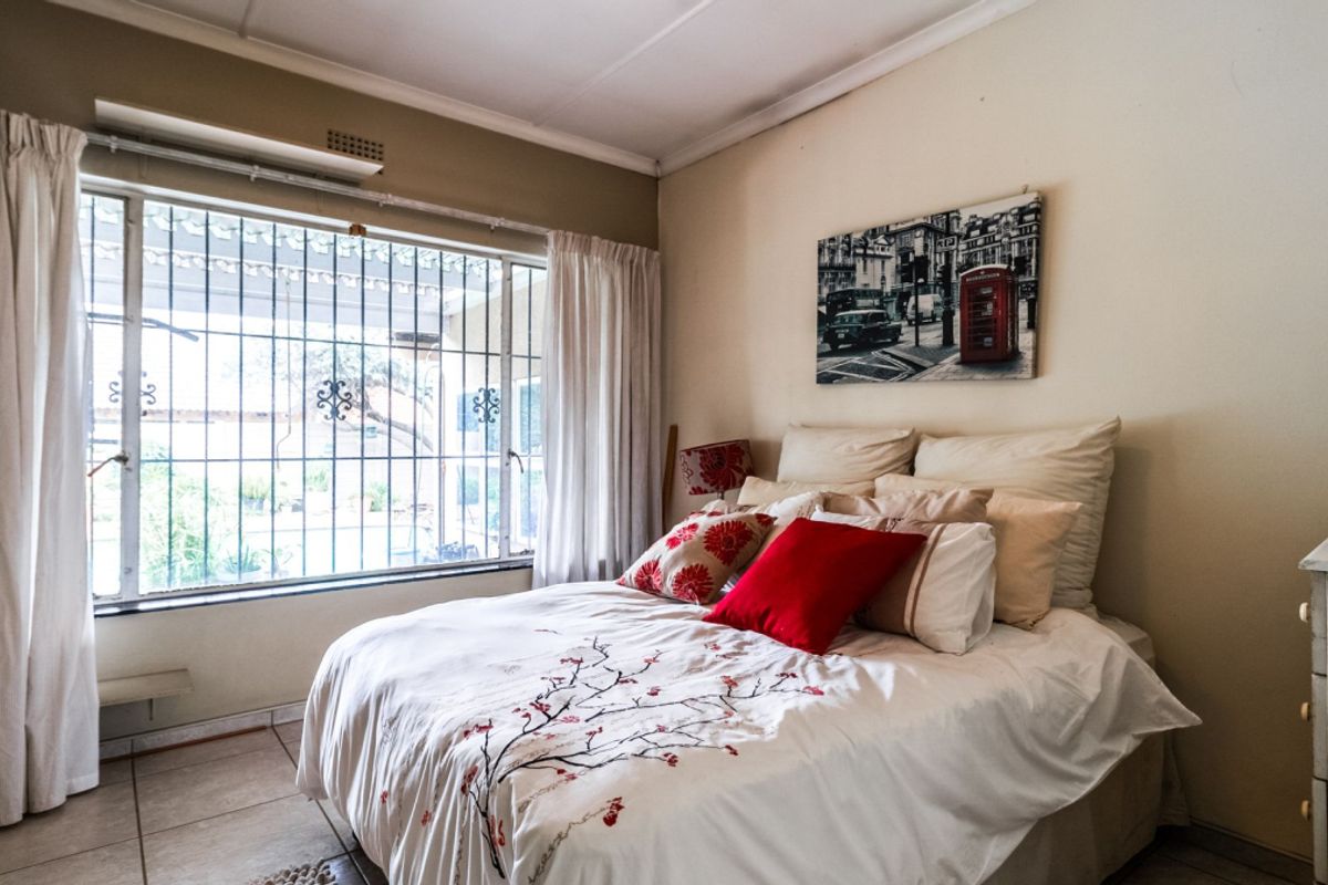 A bedroom featuring tiled flooring and a large window with integrated security bars, providing natural light and a view of the exterior.