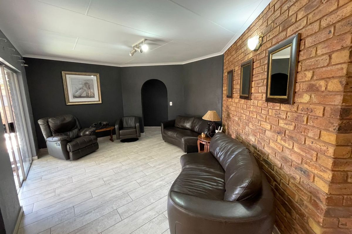 Spacious living room featuring a prominent exposed brick feature wall, tiled flooring, and an arched doorway leading to adjacent living areas.