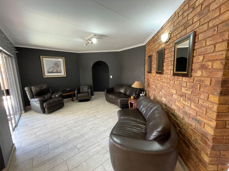 Spacious living room featuring a prominent exposed brick feature wall, tiled flooring, and an arched doorway leading to adjacent living areas.