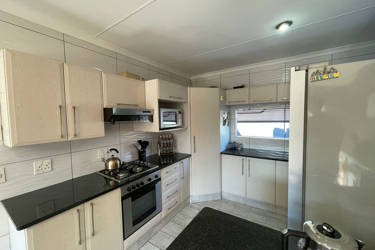 A functional kitchen featuring light wood cabinetry, dark granite countertops, a built-in gas hob, oven, and extractor fan with tiled splashbacks.