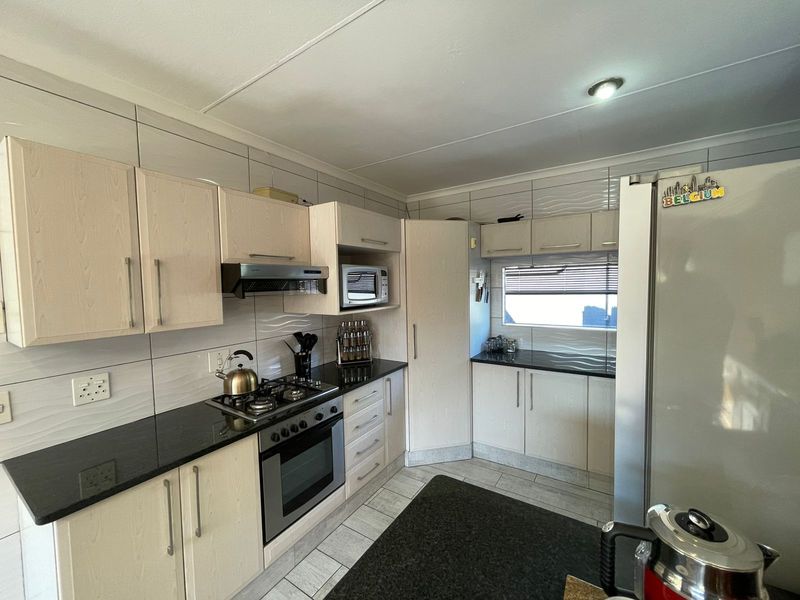 A functional kitchen featuring light wood cabinetry, dark granite countertops, a built-in gas hob, oven, and extractor fan with tiled splashbacks.