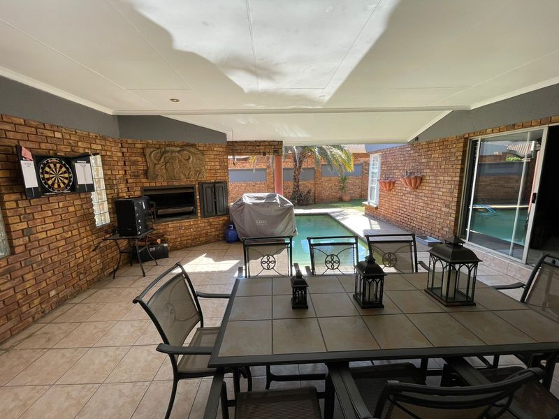 Covered patio area featuring a built-in brick braai, tiled flooring, and direct access to the swimming pool and garden.
