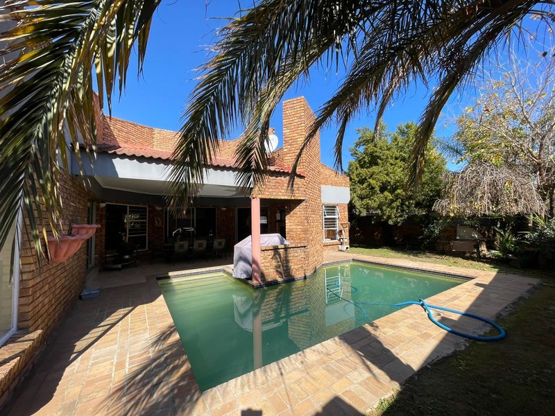 Rear exterior view featuring a brick-built house, a covered patio area, and a swimming pool set within a garden.