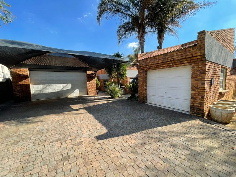 A paved driveway area featuring a double garage with a shade sail and an additional single garage, showcasing face-brick exterior finishes.