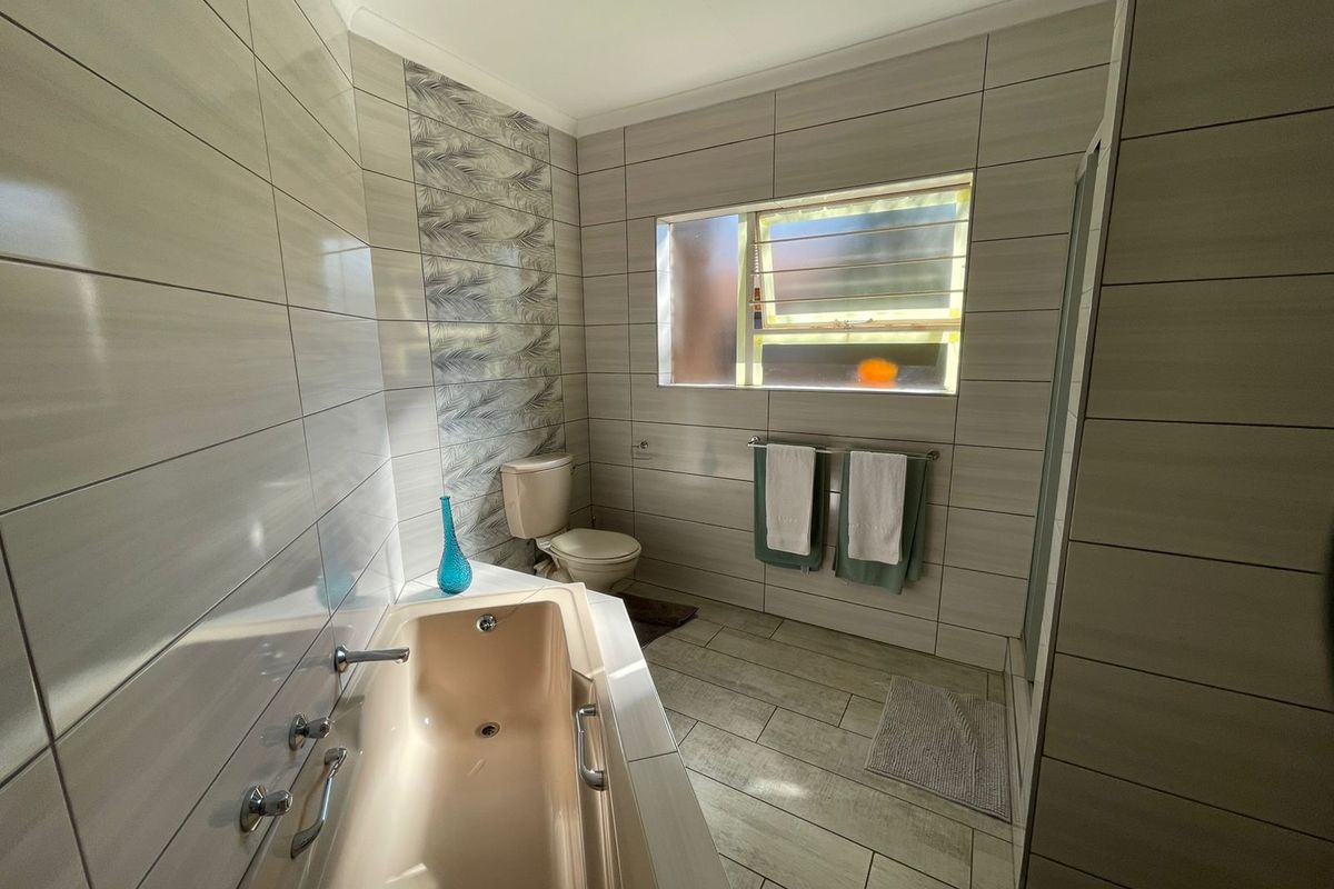 A functional bathroom featuring a built-in bathtub, toilet, and tiled walls with a decorative accent panel and a window for natural light.