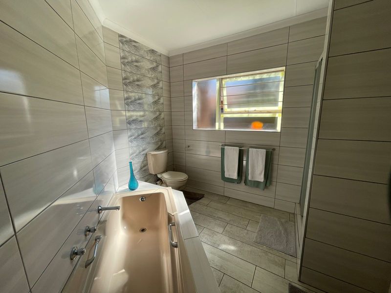 A functional bathroom featuring a built-in bathtub, toilet, and tiled walls with a decorative accent panel and a window for natural light.