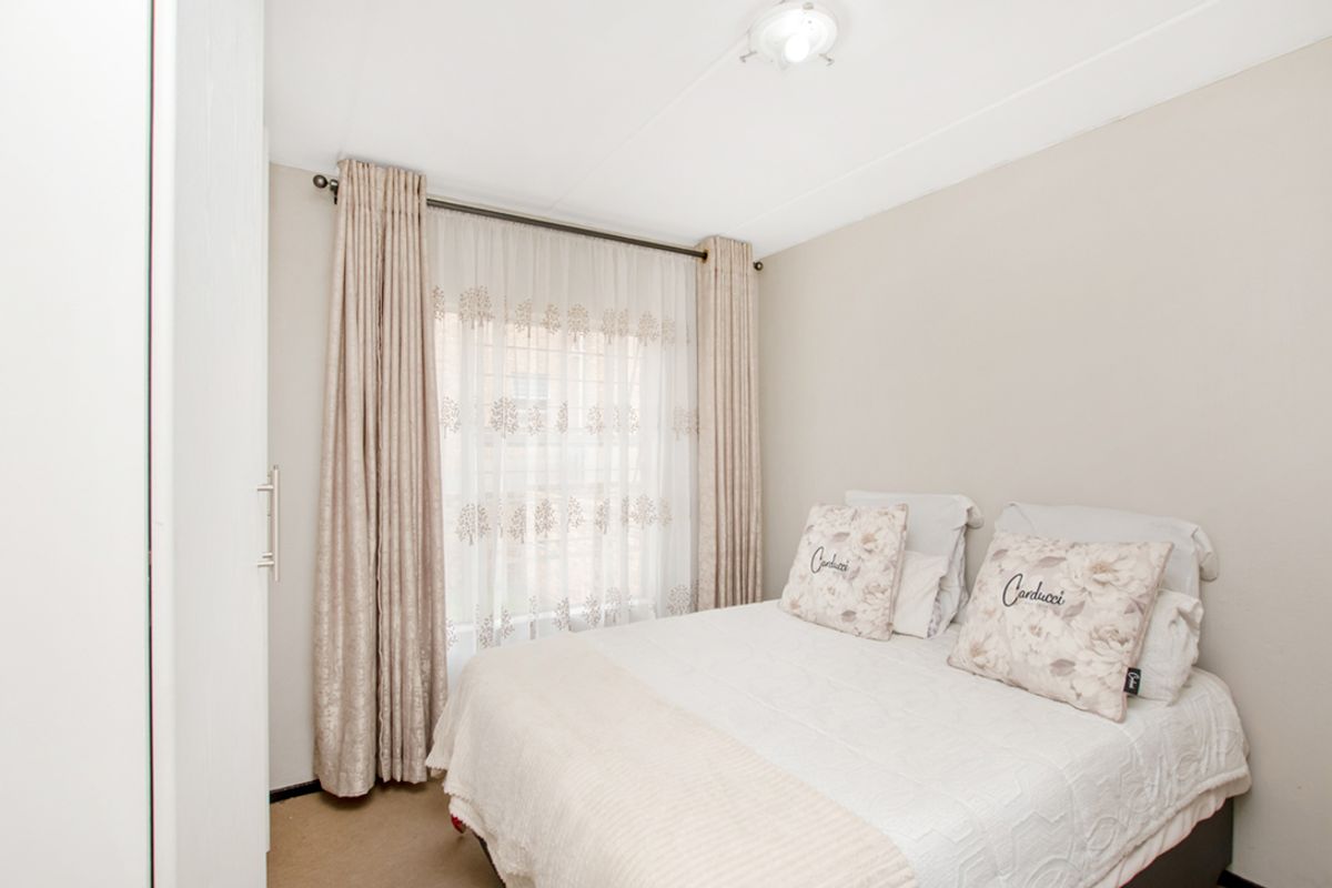 A well-lit bedroom featuring neutral wall tones, carpeted flooring, and built-in wardrobe storage.