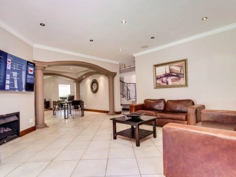 Spacious open-plan living area featuring tiled floors, decorative columns, an archway leading to a dining space, and a built-in fireplace.