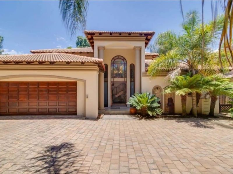 A well-maintained front elevation featuring a paved driveway, double garage, and an elegant arched entrance with architectural columns.