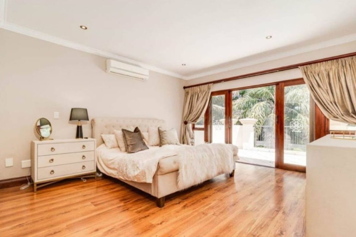Spacious bedroom featuring warm hardwood flooring, recessed lighting, a wall-mounted air conditioning unit, and large sliding glass doors providing access to an outdoor area.