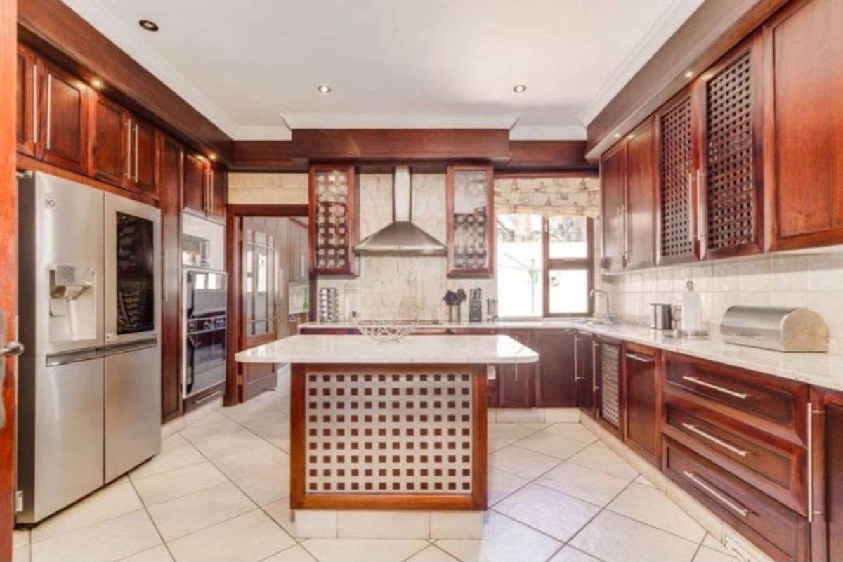 A spacious kitchen featuring dark wood cabinetry, stone countertops, a central island, and built-in stainless steel appliances with tiled flooring.