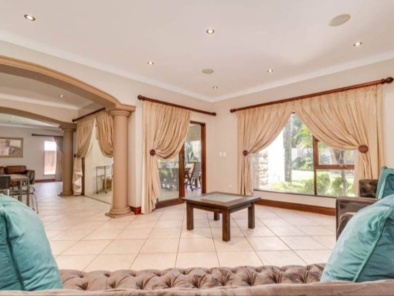Spacious open-plan living area featuring ceramic tile flooring, decorative columns, and large windows providing natural light and garden views.