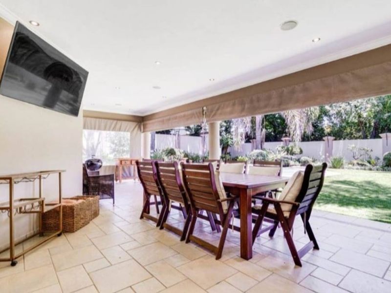 Spacious covered patio featuring tiled flooring, recessed lighting, and retractable blinds, offering a seamless transition to the landscaped garden area.