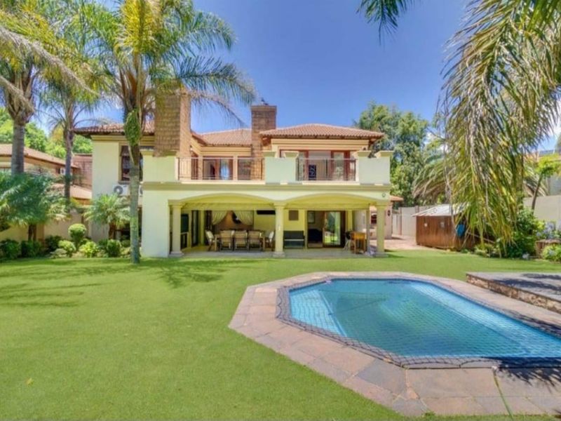 Rear view of the property featuring a spacious covered patio, upper balcony, swimming pool, and a well-maintained landscaped garden.