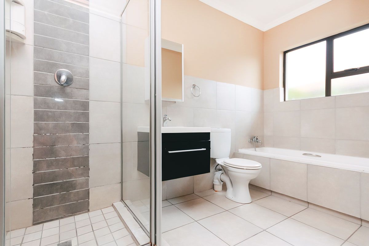 A well-appointed bathroom featuring a glass-enclosed shower, a built-in bathtub, a modern vanity, and a toilet with neutral wall and floor tiling.