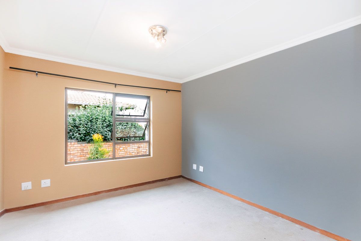 A bright, empty bedroom featuring neutral-toned walls, a large window with garden views, and carpeted flooring.