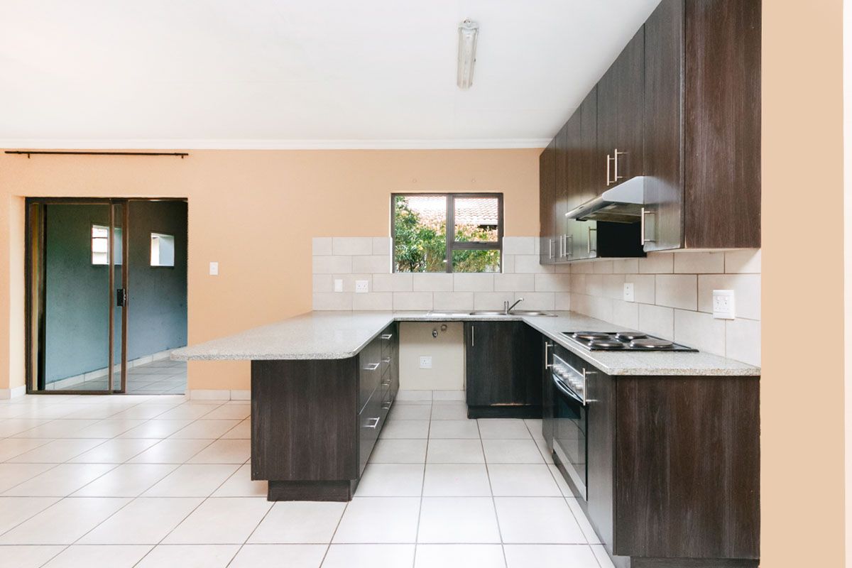 A functional kitchen featuring dark wood cabinetry, granite countertops, a built-in oven with hob, and tiled flooring with direct access to an adjacent room.