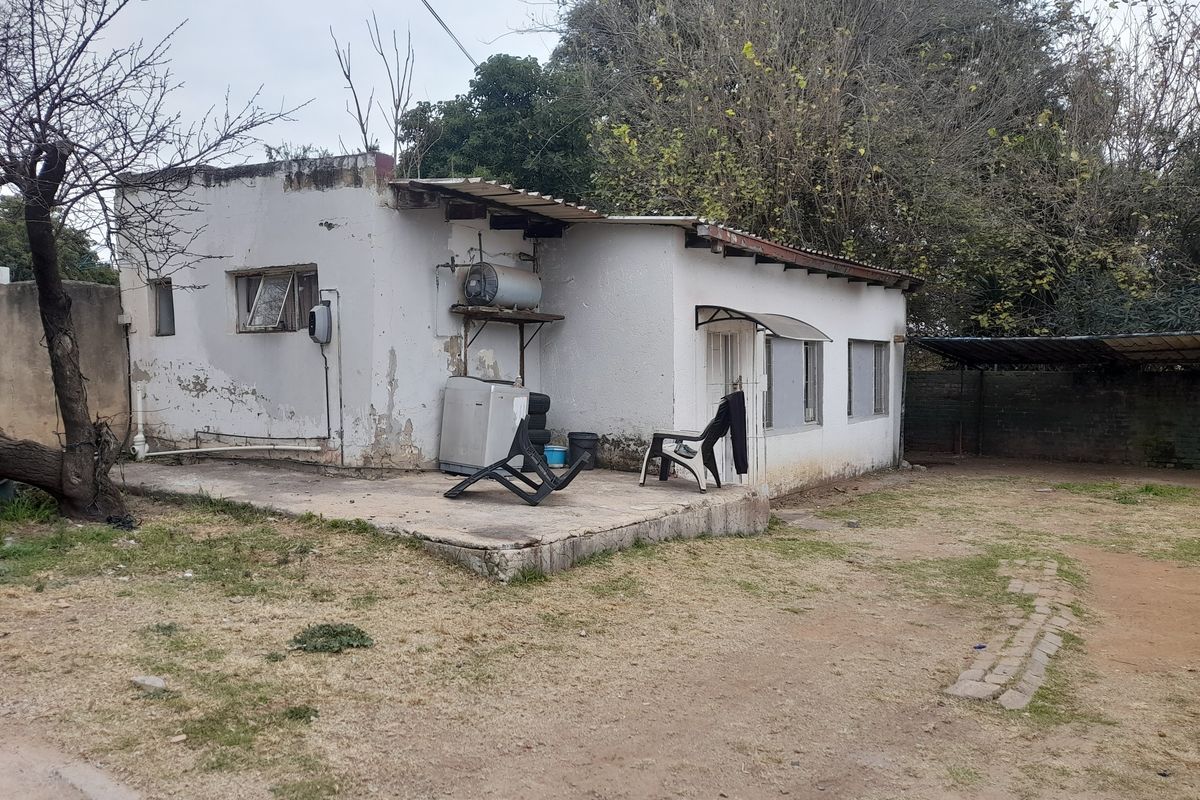 Rear view of a detached house featuring a concrete patio, external geyser, and weathered exterior walls requiring maintenance and repair.