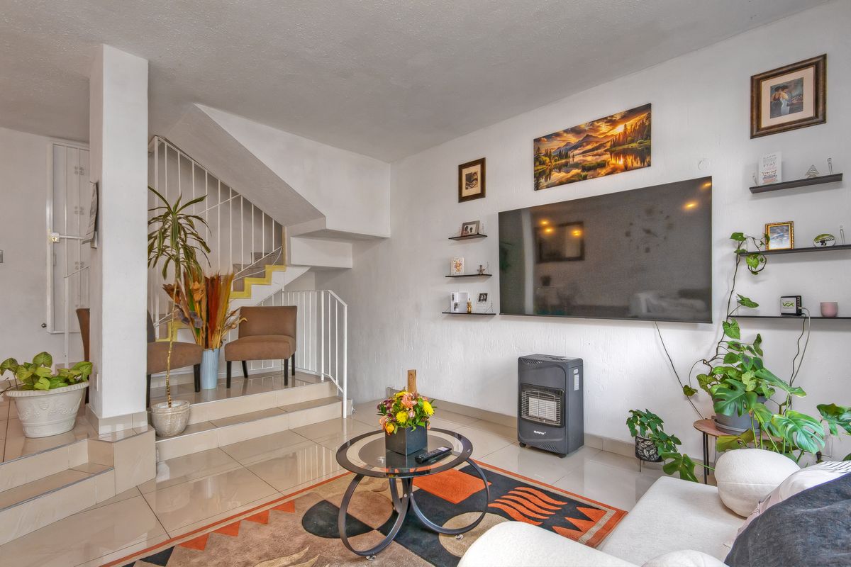 A living room featuring tiled flooring, a staircase with metal railings, and a wall-mounted television setup.