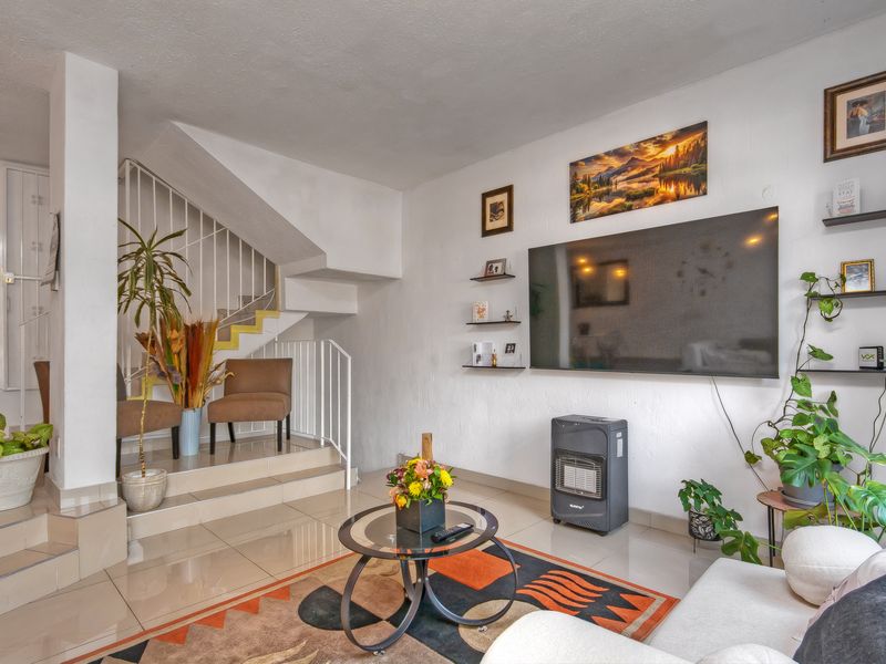 A living room featuring tiled flooring, a staircase with metal railings, and a wall-mounted television setup.