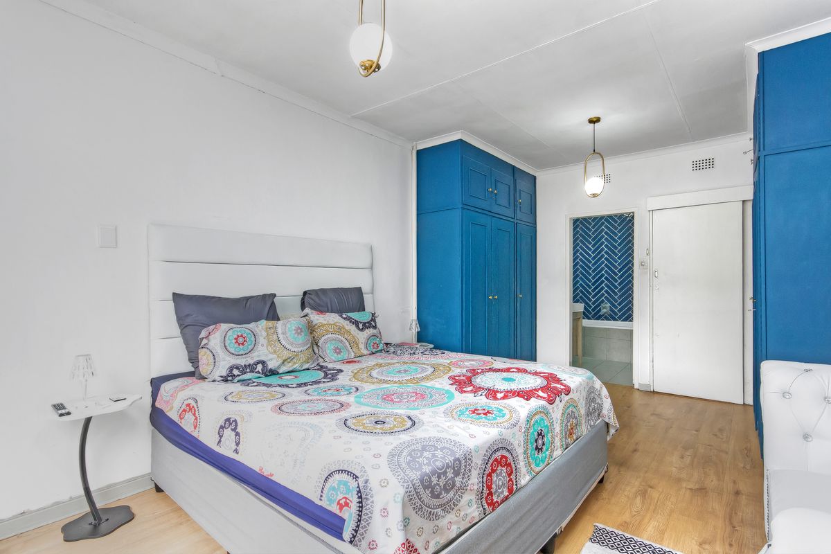 A bedroom featuring built-in blue cabinetry, wood-look flooring, and an en-suite bathroom entrance with herringbone tile accents.