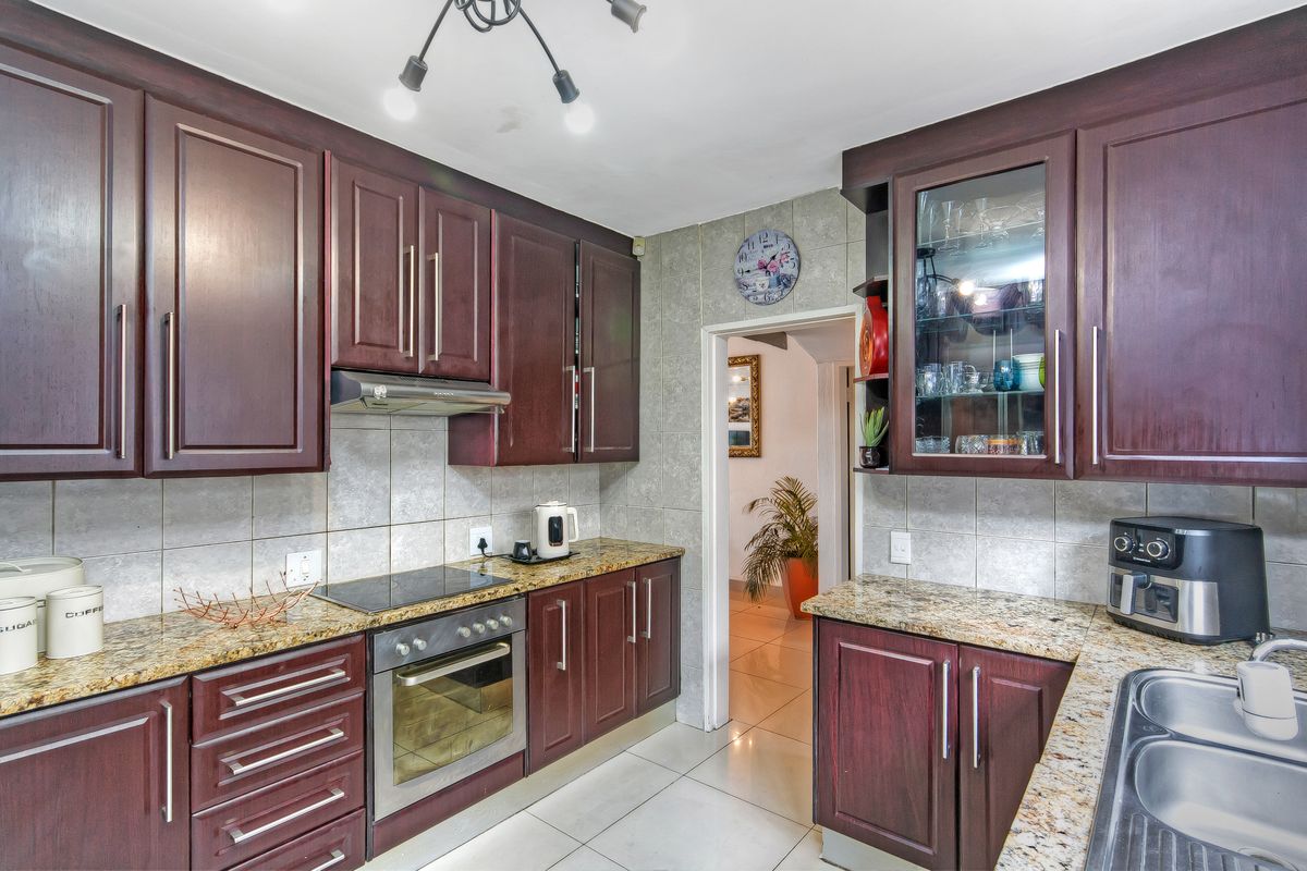 A functional kitchen featuring dark wood cabinetry, granite countertops, a built-in oven, electric hob, extractor fan, and a double stainless steel sink.