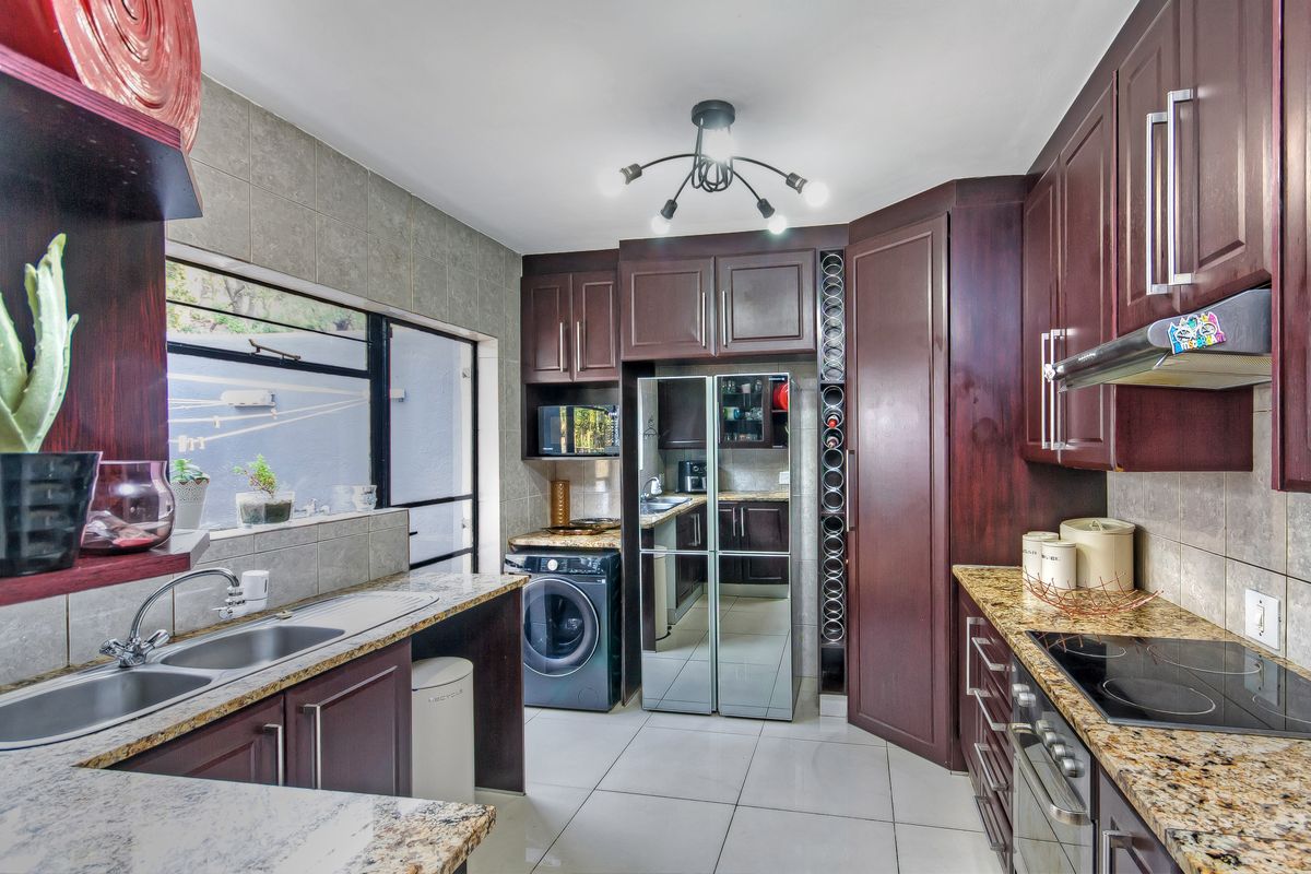 A functional kitchen featuring dark wood cabinetry, granite countertops, a built-in oven, hob, extractor fan, and integrated laundry space.