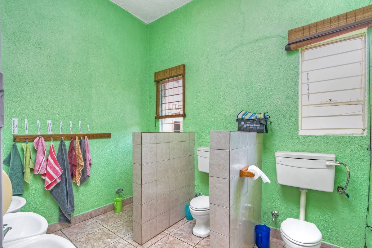 A functional bathroom featuring multiple toilets with tiled privacy partitions, tiled flooring, and bright green textured walls.