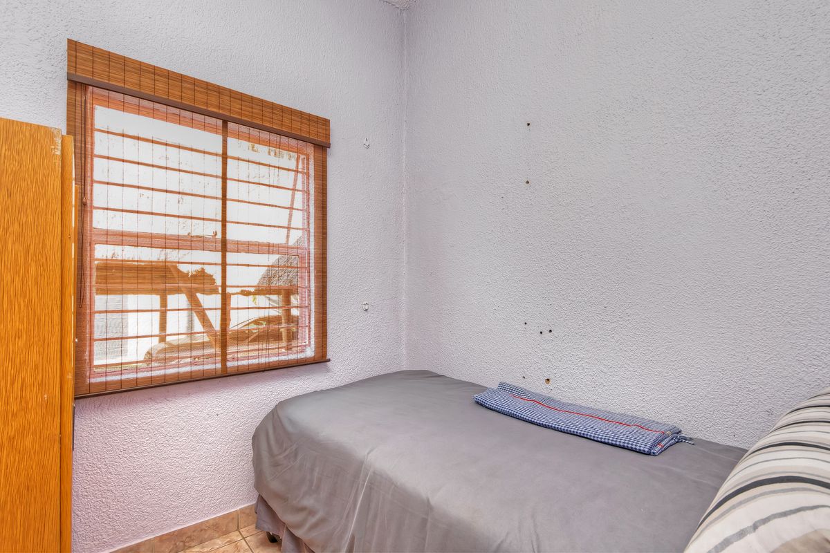 A compact bedroom featuring tiled flooring and a window with a bamboo blind, requiring minor cosmetic wall repairs.