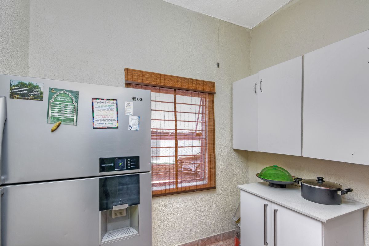 A compact kitchen area featuring basic white cabinetry, tiled flooring, and a window with a bamboo blind.