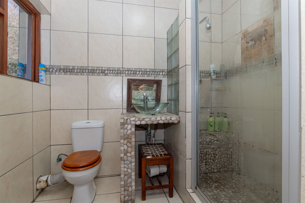 A compact bathroom featuring a glass vessel sink, tiled shower enclosure with pebble flooring, and a standard toilet.